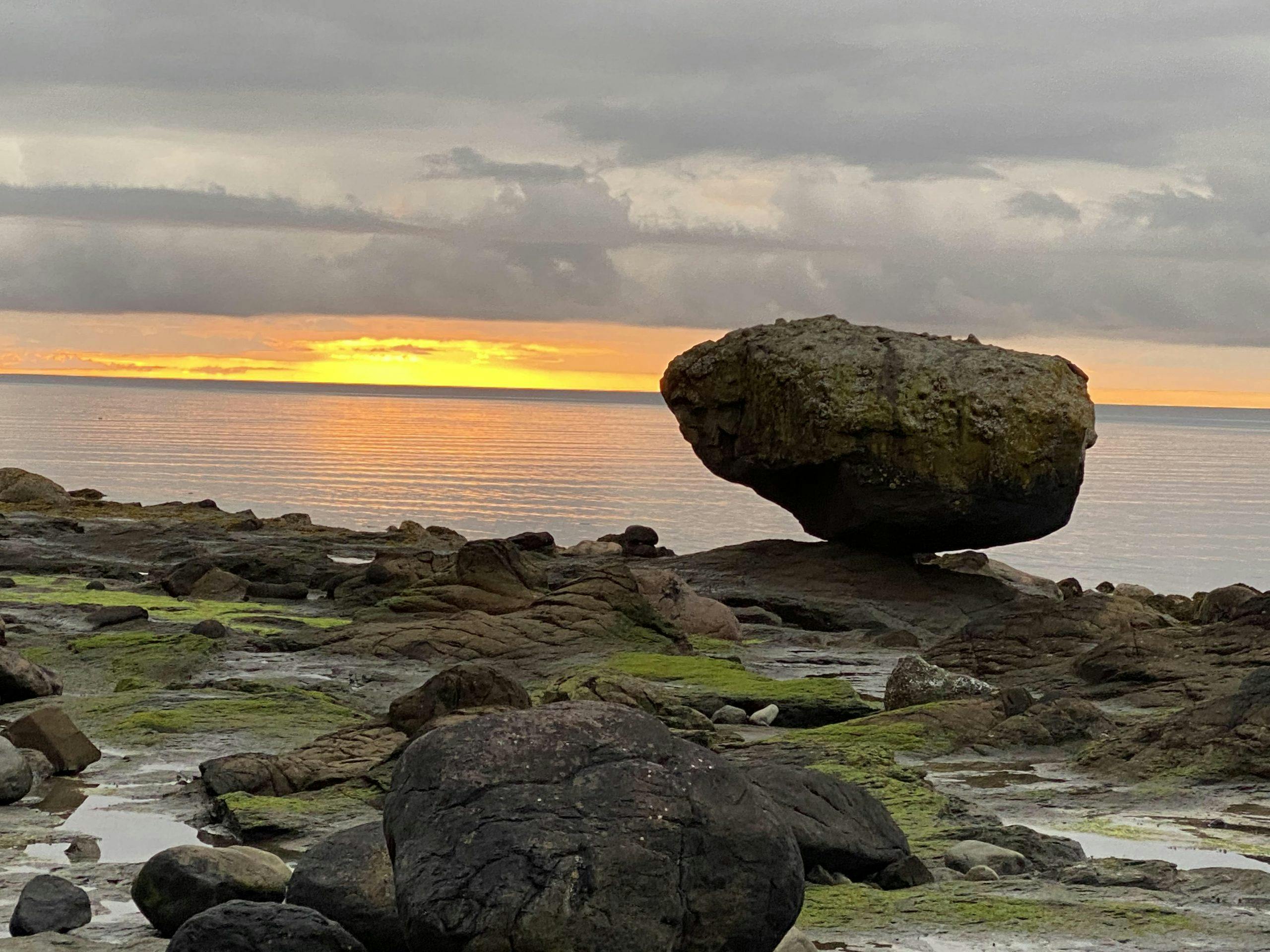 Photo of a boulder balancing precariously on the beach.
